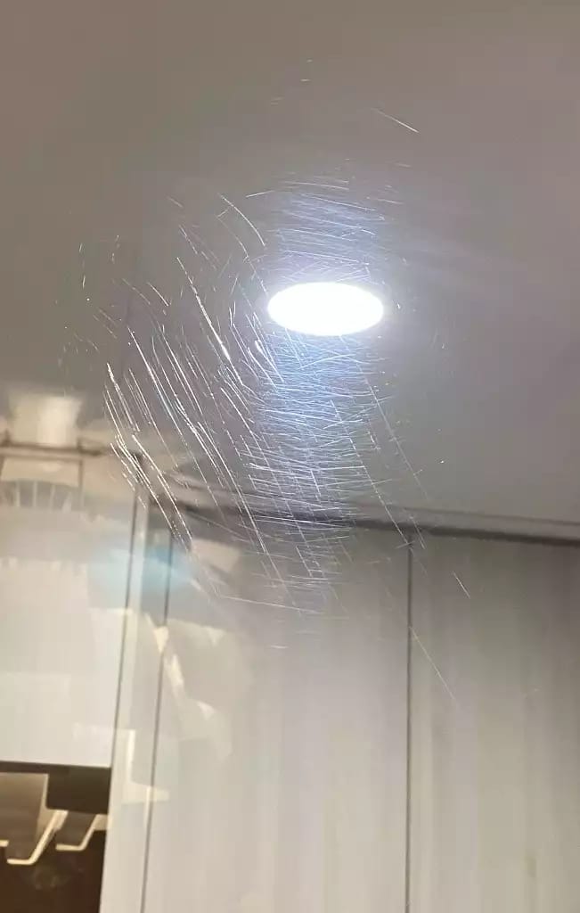 Fine crossing scratches visible around the reflection of a round ceiling light