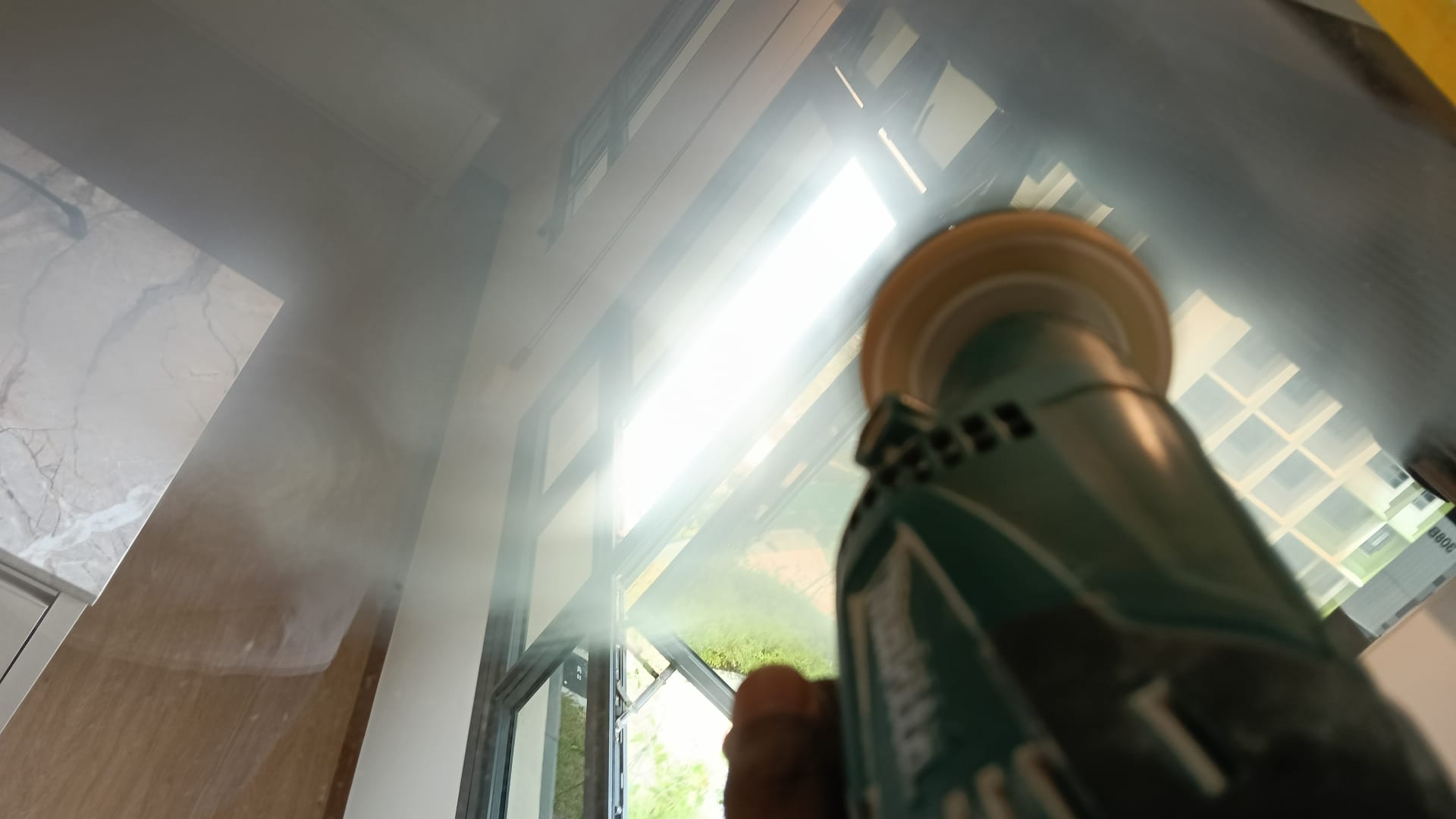 A handheld tool with a round pad against an installed glass panel