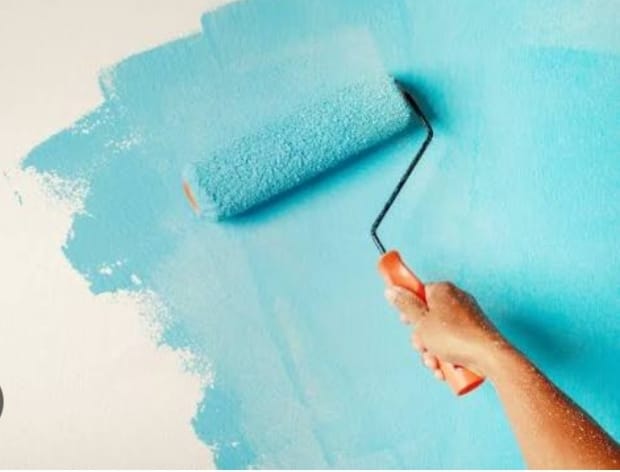 A hand rolling turquoise paint onto a white wall