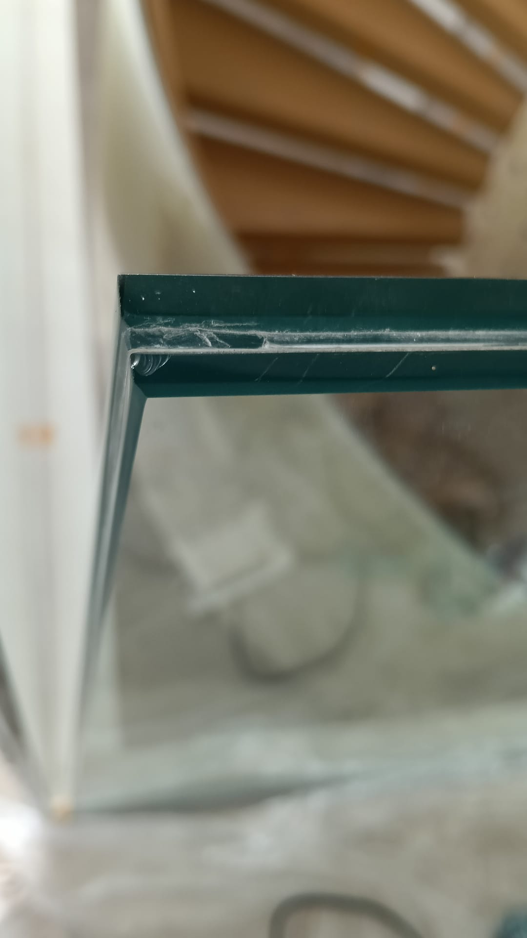 Close-up of a glass corner with an irregular edge area, beside timber stairs