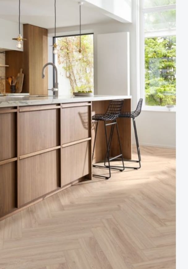 Light oak-tone herringbone flooring beside a timber kitchen peninsula and two bar stools